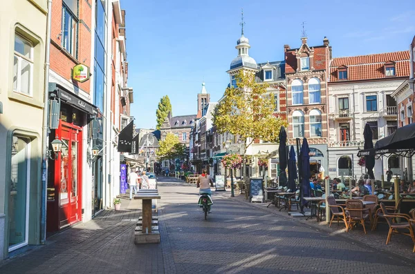 Venlo, Limburg, Hollandia - 2018. október 13.: Street with cafes, restaurants, and bars in the historical center of the Dutch city. Egy nő biciklizik. Városi biciklizés. Vízszintes fénykép — Stock Fotó