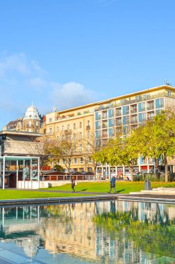 Budapest, Hungary - Nov 6, 2019: Streets of Hungarian capital city with trees in the fall colors. Water from fountain in the foreground. Vertical photo