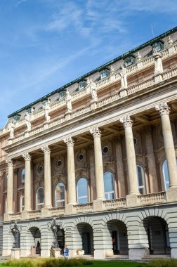 Budapeşte, Macaristan - 6 Kasım 2019: Buda Kalesi 'ndeki binanın dikey fotoğrafı. Tarihi saray binası, sütunlu ve kemerli pencereli cephe. Binanın önündeki insanlar..