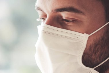 Koronavirüs karantinası sırasında tıbbi maske takan sakallı beyaz bir adamın fotoğrafını çek. Yüzün ön kısmı hafifçe bulanıklaştı. Coronavirus, COVID-19 salgını. Doktor, hemşire konsepti.