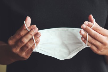 Beyaz tıbbi maske takan kadın eller. Coronavirüs salgını sırasında karantinada olan bir kadın. Yakın plan, arka plan bulanık. COVID-19 salgını. Coronavirus konsepti, kavramsal fotoğraf.