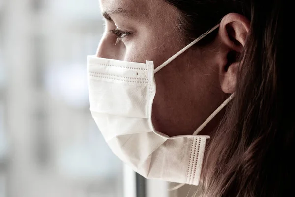 Gribi önlemek için beyaz tıbbi maske takan beyaz saçlı genç bir kadının ayrıntıları. Yüzün ön kısmına odaklan, arka plan bulanık. Coronavirus, COVID-19 karantinası. Doktor, hemşire konsepti.