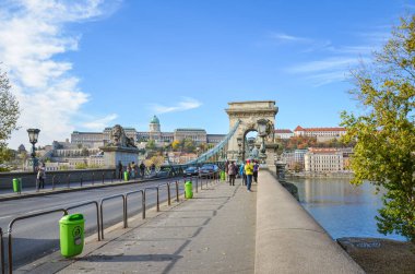 Budapeşte, Macaristan - 6 Kasım 2019: Ünlü Szechenyi Zinciri Köprüsü, asma köprü, Macaristan 'ın başkentindeki Tuna Nehri üzerinde. Turistler etrafı geziyor, arabalar yolda gidiyor. Buda Kalesi arka planda.