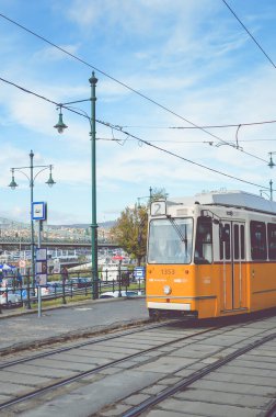 Budapeşte, Macaristan - 6 Kasım 2019: Bir tramvay istasyonunda sarı tramvay. Szechenyi zincir köprüsü ve arka plandaki tarihi merkez. Macar toplu taşımacılığı. Filtreli dikey fotoğraf.