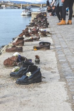 Budapeşte, Macaristan - 6 Kasım 2019: Demir Ayakkabılar Tuna Bankası 'nda. 2. Dünya Savaşı sırasında faşistler tarafından öldürülen Yahudilerin anıtı. Tuna 'yı ve arkada turistleri bulanıklaştırdı. Dikey fotoğraf.