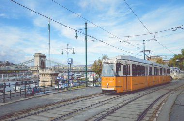 Budapeşte, Macaristan - 6 Kasım 2019: Bir tramvay istasyonunda sarı tramvay. Szechenyi zincir köprüsü ve arka plandaki tarihi merkez. Macar toplu taşımacılığı. Filtreli yatay fotoğraf.