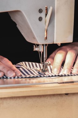 Kadın elleri, koronavirüs salgını sırasında yüz maskesi dikmek için dikiş makinesini kullanıyor. Virüse karşı ev yapımı koruyucu maske. Dikiş maskeleri, COVID-19.