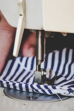 Kadın elleri, koronavirüs salgını sırasında renkli bir yüz maskesi dikmek için dikiş makinesini kullanıyor. Virüse karşı ev yapımı koruyucu maske. Dikiş maskeleri, COVID-19. Seçici odak.