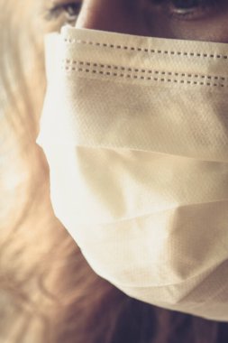 Beyaz bir tıbbi maske takan beyaz bir kadının ayrıntıları. Üzgün ve yorgun görünüyorsun. Yüzün ön kısmına odaklan, arka plan bulanık. Coronavirus, COVID-19 karantinası. Hemşire kavramı. Dikey fotoğraf.