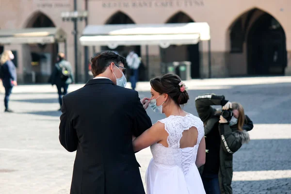 Prag, Çek Cumhuriyeti - 23 Nisan 2020: Sağlık maskeli düğün çifti eski kentte yüz maskeli fotoğrafçılar tarafından fotoğraflanıyor. Koronavirüs salgını sırasında düğün. COVID-19 Düğünleri.