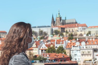 Çek Cumhuriyeti Prag 'daki Charles Köprüsü' nde tıbbi maskeli genç bir kadın. Arka planda bulanık eski kasaba ve Prag Kalesi. Seyahat, Coronavirus sırasında turizm. COVID-19. Yatay fotoğraf.