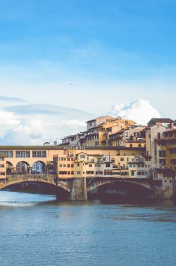 Ünlü Ponte Vecchio Köprüsü, Floransa, Toskana, İtalya 'daki Arno Nehri üzerindeki ortaçağ taş köprüsü. İtalyan şehrinin büyük simgesi. Mavi gökyüzü, arka planda bulutlar. Dikey fotoğraf.