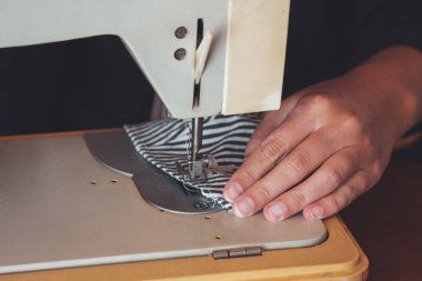 Kadın elleri, koronavirüs salgını sırasında yüz maskesi dikmek için dikiş makinesini kullanıyor. Virüse karşı ev yapımı koruyucu maske. Dikiş maskeleri, COVID-19. Kısmen bulanık, seçici odaklanma.
