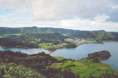 Portekiz 'in Azores kentindeki Miradouro do Cerrado das Freiras bölgesinden Lagoa Azul ve köy Sete Cidades' in muhteşem manzarası. Yeşil tarlalar ve ormanlarla çevrili göller. Yatay fotoğraf.