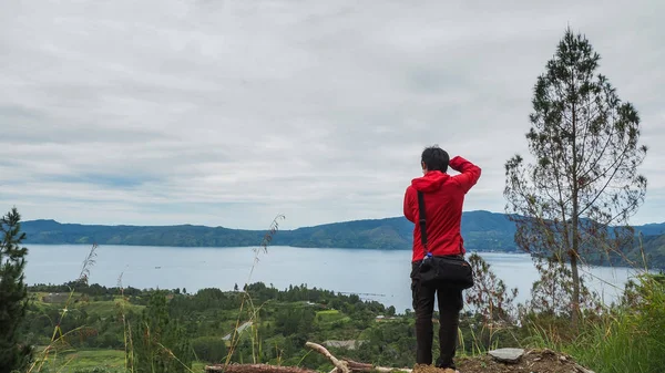 man standing on hill looking at the lake toba