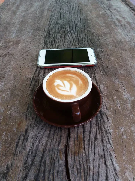 コーヒー カップでコーヒー トップ 熱いラテの泡で熱い豊かなラテ アート木製スマート フォン — ストック写真