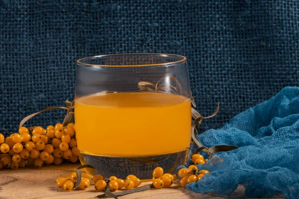 Vejetaryen yemeği, sağlıklı beslenme, olgun sulu deniz dikenlerinin hasadını koruma, taze, sağlıklı vitamin içeceği hazırlama. Meyve suyu ve turuncu deniz dikenli doğal mavi kumaşlı dallarla dolu bir bardak.