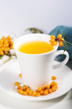 Beyaz bardakta deniz dikenli çay ve doğal peçetenin üzerinde böğürtlen. Sonbahar ve kış aylarında besin vitaminlerinin kaynağı