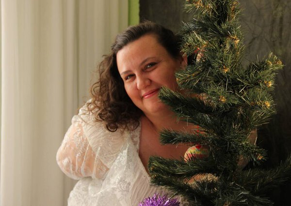 Толстая женщина украшает ёлку. Радость предстоящего праздника. Декор дерева
