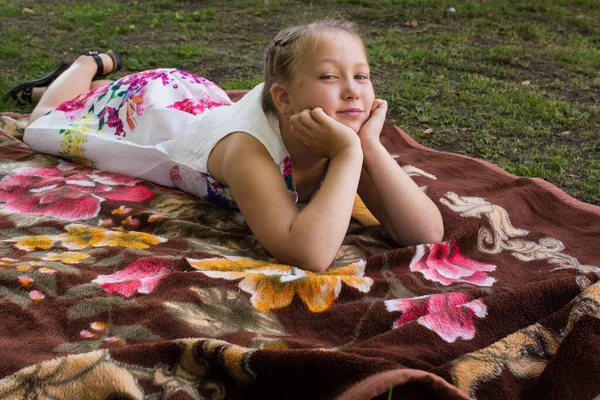 Krásná mladá dívka odpočívá na pikniku v létě. Rozprostřela pokrývku na trávu a lehla si. — Stock fotografie