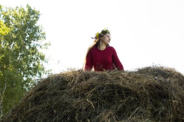 Samanlığın yanındaki sarışın kız. Başında bir çiçek çelengi. saman yapımı.