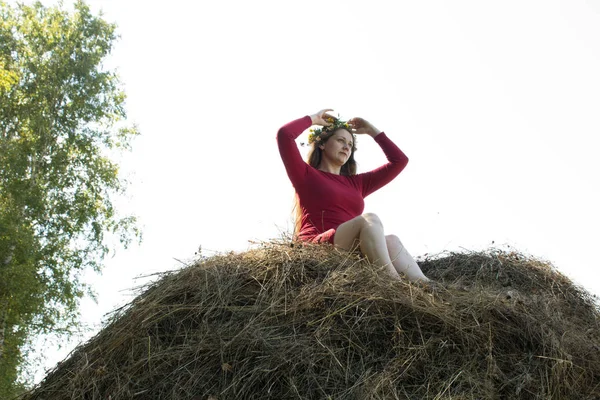 Blond flicka nära en höstack. En blomsterkrans på huvudet. hösnäring. — Stockfoto