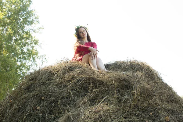 Une blonde près d'une botte de foin. Une couronne de fleurs sur la tête. fenaison . — Photo