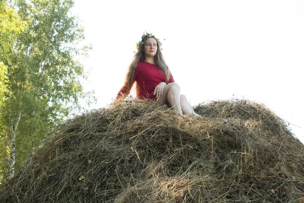 Blond flicka nära en höstack. En blomsterkrans på huvudet. hösnäring. — Stockfoto