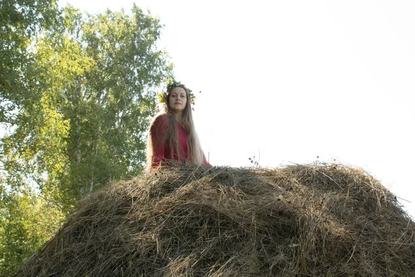 Blonde girl near a haystack. A wreath of flowers on the head. haymaking. — Stock Photo, Image