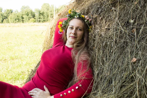 Blond flicka nära en höstack. En blomsterkrans på huvudet. hösnäring. — Stockfoto