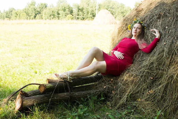 Ragazza bionda vicino a un pagliaio. Una corona di fiori sulla testa. fieno . — Foto Stock