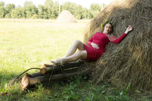 Ragazza bionda vicino a un pagliaio. Una corona di fiori sulla testa. fieno . — Foto Stock