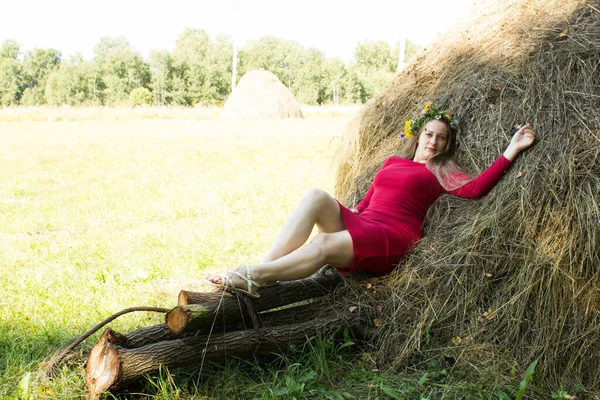 Ragazza bionda vicino a un pagliaio. Una corona di fiori sulla testa. fieno . — Foto Stock