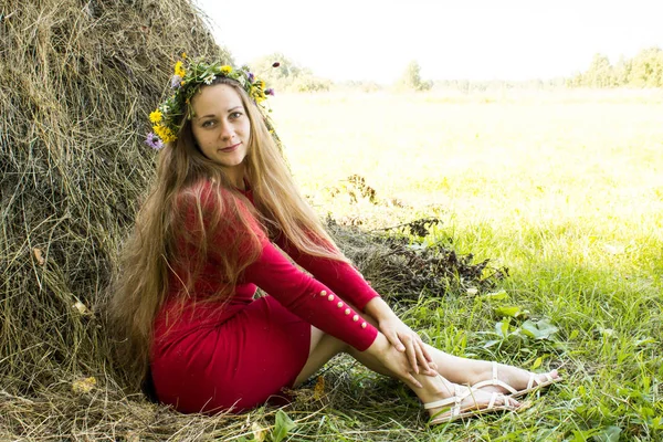 Ragazza bionda vicino a un pagliaio. Una corona di fiori sulla testa. fieno . — Foto Stock