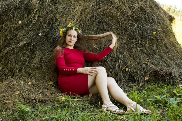 Ragazza bionda vicino a un pagliaio. Una corona di fiori sulla testa. fieno . — Foto Stock