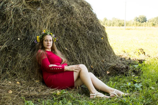 Ragazza bionda vicino a un pagliaio. Una corona di fiori sulla testa. fieno . — Foto Stock