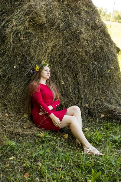 Blond flicka nära en höstack. En blomsterkrans på huvudet. hösnäring. — Stockfoto
