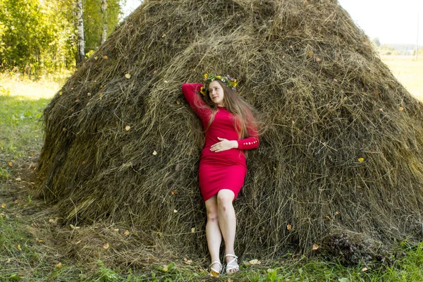 Blond flicka nära en höstack. En blomsterkrans på huvudet. hösnäring. — Stockfoto