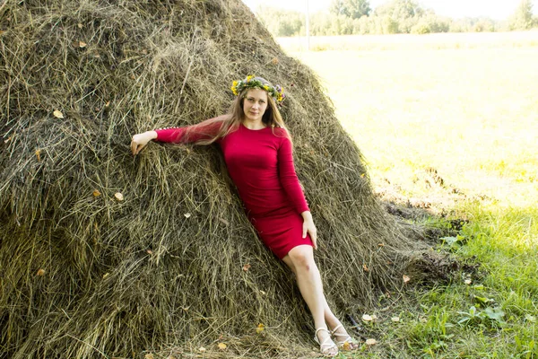 Une blonde près d'une botte de foin. Une couronne de fleurs sur la tête. fenaison . — Photo