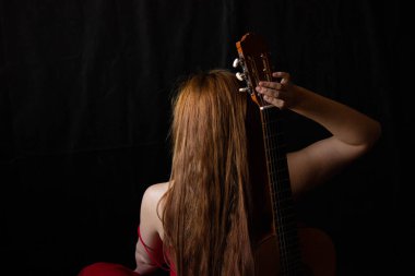 Kırmızı elbiseli kız siyah arka planda gitarın yanında oturuyor.