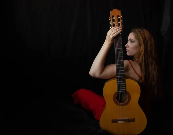 Kırmızı elbiseli kız siyah arka planda gitarın yanında oturuyor.