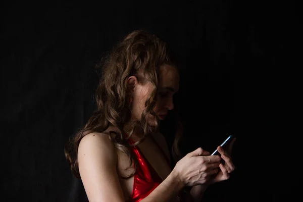 Retrato de uma menina sexy com cabelos longos em um vestido curto com umas costas abertas em um fundo preto. nas mãos do telefone — Fotografia de Stock