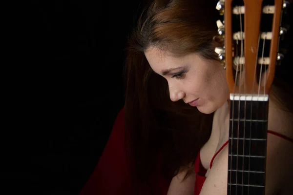 Menina em um vestido vermelho senta-se no chão perto da guitarra em um fundo preto — Fotografia de Stock