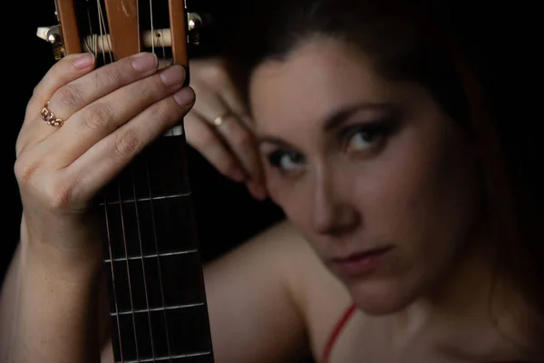 Menina em um vestido vermelho senta-se no chão perto da guitarra em um fundo preto — Fotografia de Stock