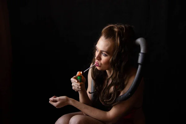 La ragazza suxual tiene una sigaretta nelle labbra, nelle mani di un accendino. Si siede su un aspirapolvere. stanco di faccende domestiche — Foto Stock