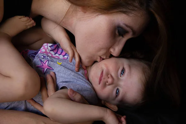 Mamma kramar med sitt barn och kysser det på svart bakgrund. Lycklig barndom. — Stockfoto