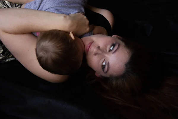 Mamma kramar med sitt barn och kysser det på svart bakgrund. Lycklig barndom. — Stockfoto