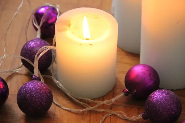 Brandende kaarsen naast paarse slinger ballen. — Stockfoto