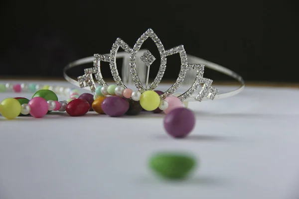 Silver tiara next to children's multicolored beads and sweets in multi-colored glaze — Stock Photo, Image