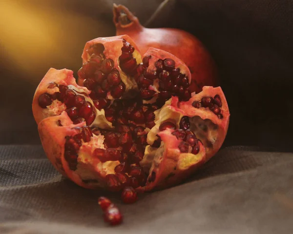 Open grenade lies against a black background. red grains glisten. dark-key macro photography. — Stock Photo, Image